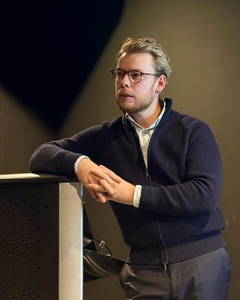 Fabian Schmidt bei einem Vortrag in Boston, an ein Pult gelehnt